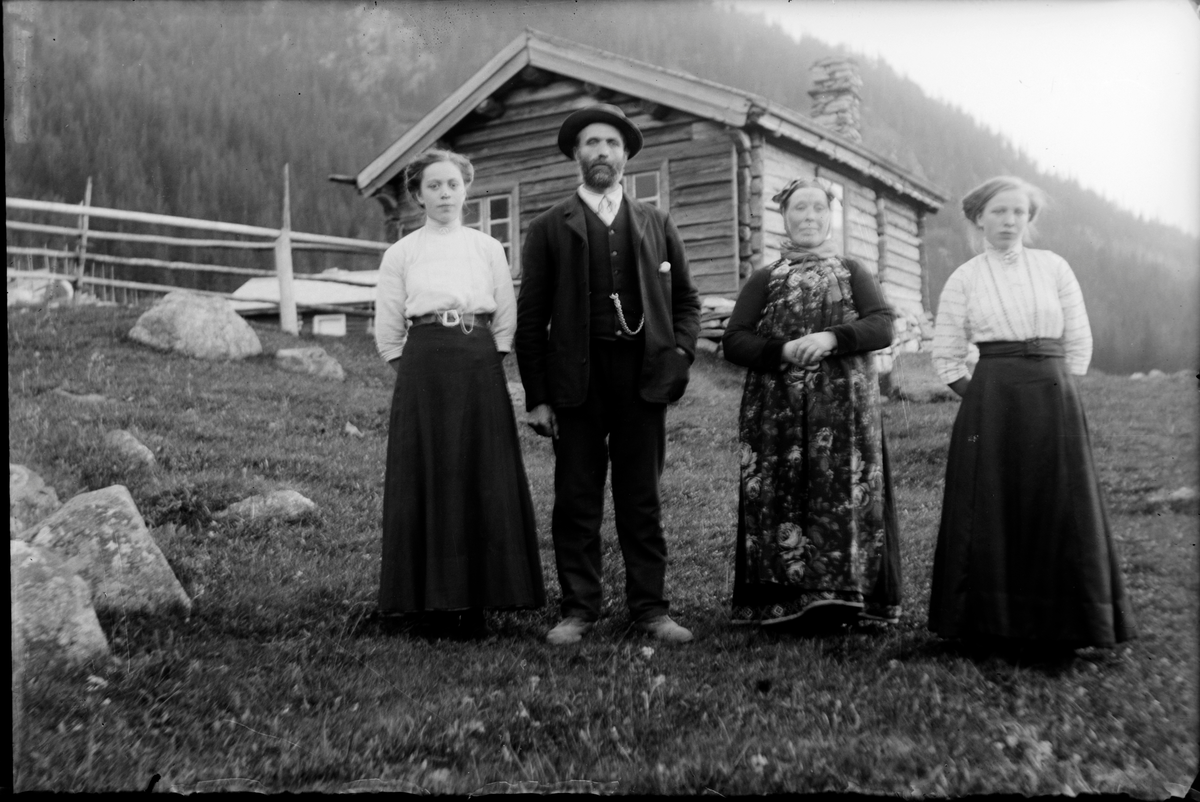 Familien fra Vissebråten . Lars og Eli Vissebråten med døtrene Borghild og Barbo. Eli i hallingbrunad og korttrøye de andre i finklær. I bakgrunn et tømmerhus.
