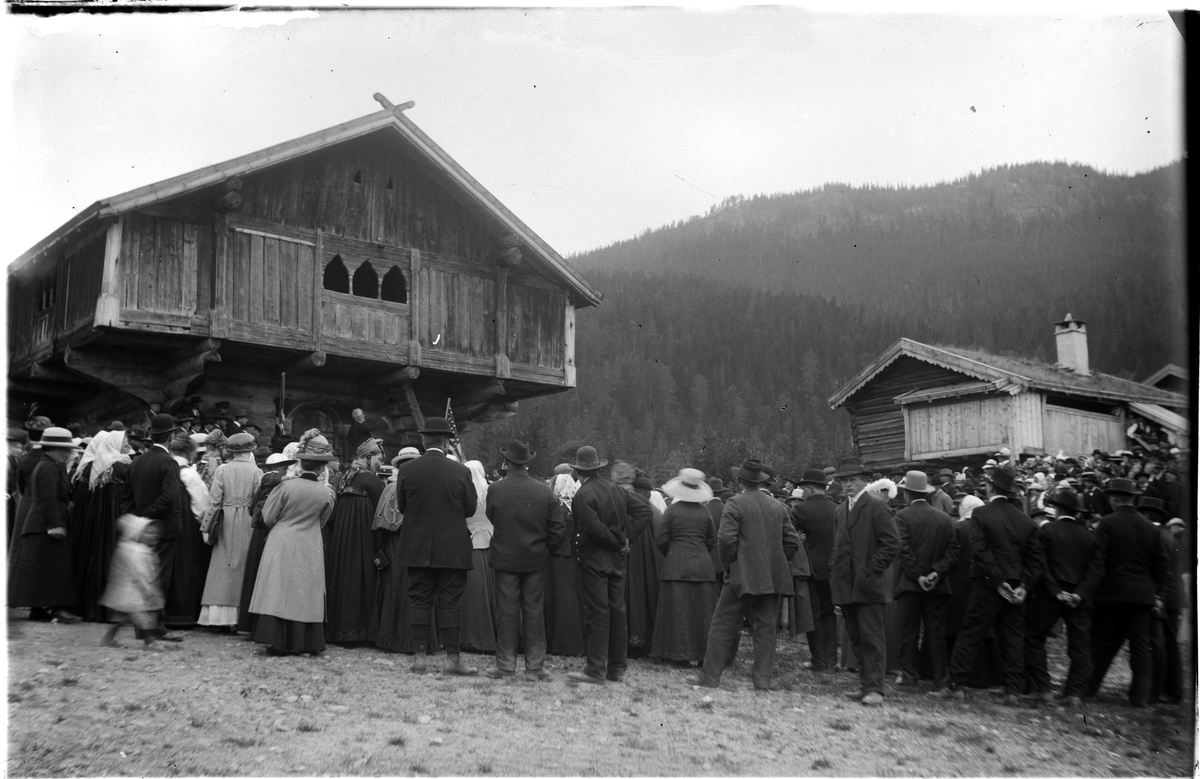 Forsamling på museumsområdet
Forsamling  foran Staveloftet og Trøimstugu. Mange i bunad,side drakter og mennene i dress.  Overlevering av fane til Hallingslaget 31. mai 1914, 1. pinsedag.
