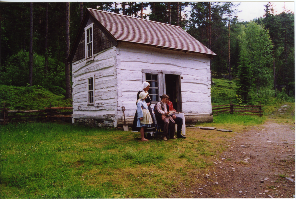 Emigrantspelet. Gammel kone med barn ved amerikahuset.
