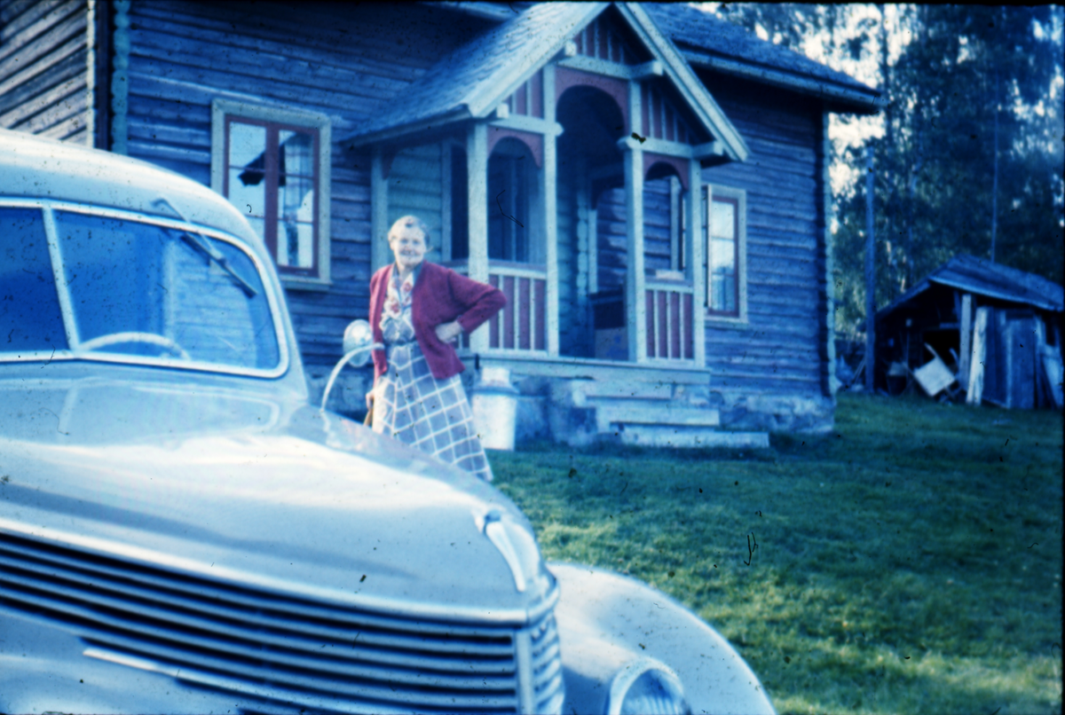 Hallingstugu med veranda (kårstugu) i Øvre Børdalen. T.v. fronten på bilen til Knut Smette en Ford 1938 modell. Dama i bildet er Gunhild Børdalen.
