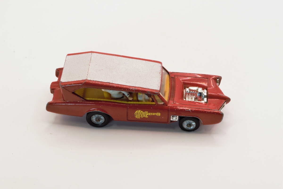 Rød lekebil fra 60/70-tallet. Produsert i Wales. The Monkeemobil. Modell av Dean Jeffries 1966 Pontiac GTO som var med i den amerikanske TV-serien The Monkees. Fire figurer i setene som spiller gitar og vinker, karakterene i serien spiller i band.