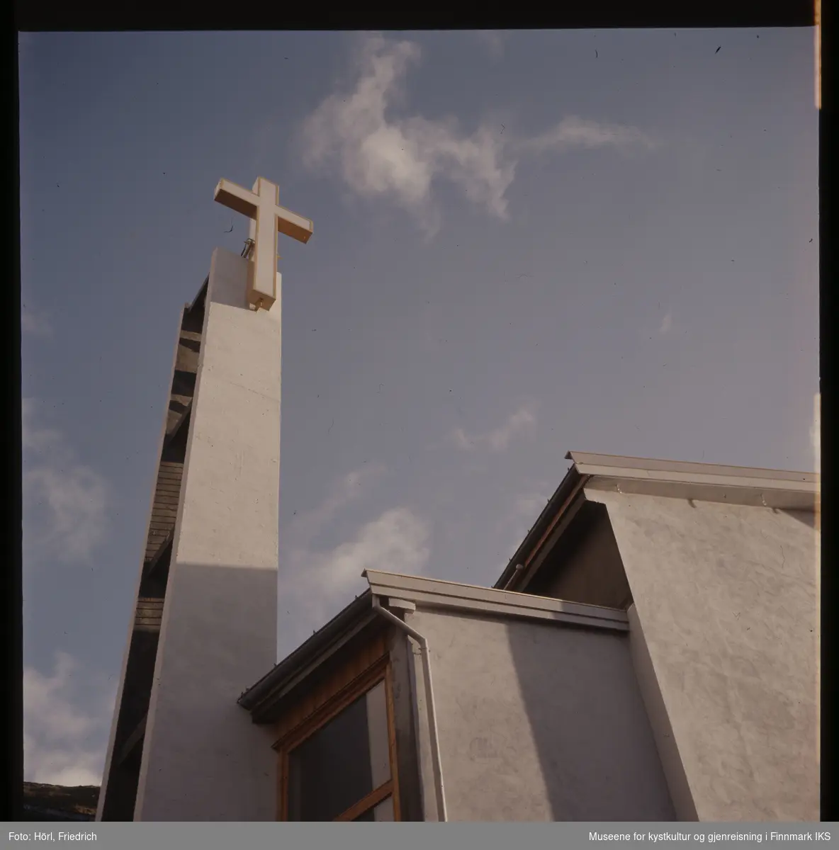 Klokketårnet til den nye katolske kirke St. Mikael i Hammerfest har reist seg og toppes av et stort, lyssatt kors. Himmelen er lett skyet.