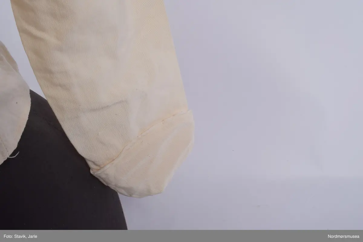 Skjorte i naturhvit lin med påsydd blondekrage. kragestoffet er påsydd slik at omtrent halvparten går nedenfor kragen, mens resten danner kragen. Trykknapper i ryggen. Ermene er laget for å brettes lett opp i enden. I front er stofet brett og deretter sydd i en stripe som går fra skulderen ned til livet. Denne stripen fortsetter på baksiden på samme vis. To ekstra striper i front. Tre stoffkledde pynteknapper er plassert øverst ved hver stripe. Bortsett fra enkelte påsydde stoffbiter slik som innlegg under armene ser skjorten ut til å være laget av ett stoffstykke tilklipt i form.