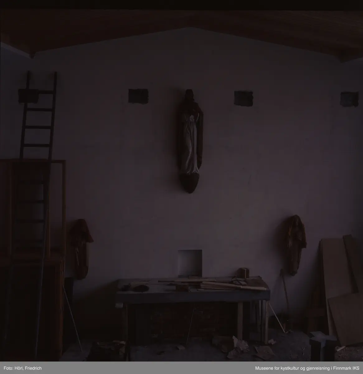Fotografiet er noe underbelyst. Den viser interiøret av Den katolske kirke St. Mikael i Hammerfest i byggeperioden. Alteret er under byggingen. Skulpturene på veggen til venstre og høyre for det er dekket med tepper. Til venstre i bildet skimter man en lang stige som er lent mot veggen.