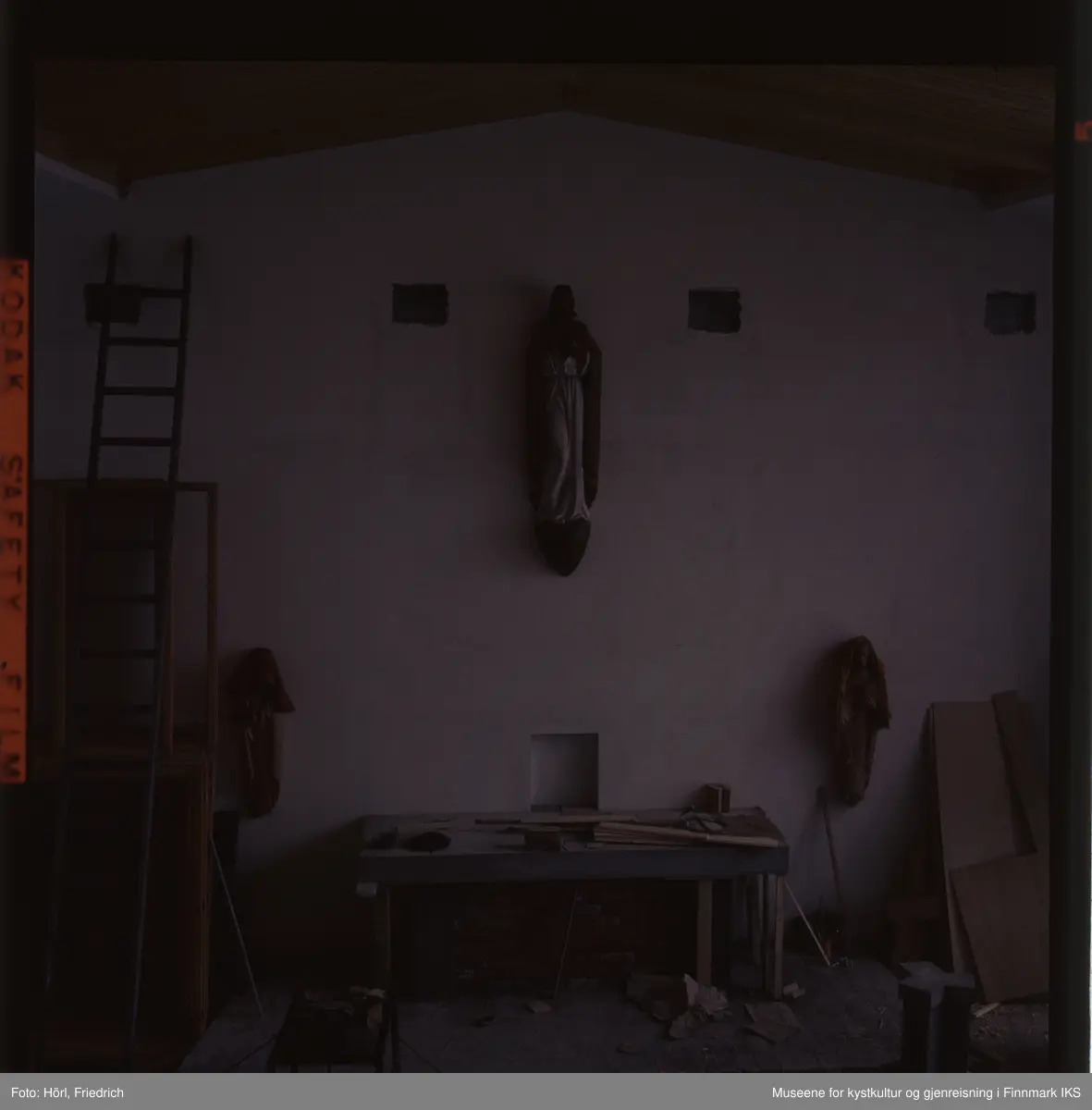 Fotografiet er noe underbelyst. Den viser interiøret av Den katolske kirke St. Mikael i Hammerfest i byggeperioden. Alteret er under byggingen. Skulpturene på veggen til venstre og høyre for det er dekket med tepper. Til venstre i bildet skimter man en lang stige som er lent mot veggen.