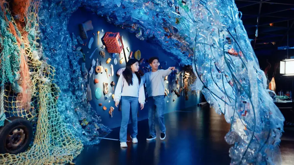 Children walking under a large blue wave made of plastic in the Explore the Ocean exhibition at the Norwegian Maritime Museum.