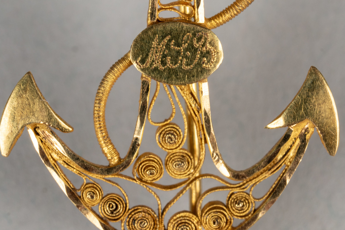 Nål i gullfiligrans, formet som et anker. Dekorert med monogram