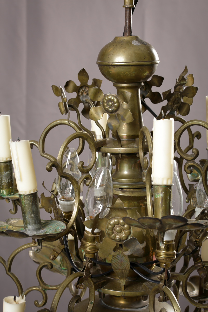 En ljuskrona av mässing, tolvarmad och försedd med anbringbara ornamenter. Kronan har profilerad mittstång, ändklot och tolv s-formade ljusarmar med cylindriska pipor och musselformade droppskålar. Reflexornamenten är blomformade. Ljuskronan är försedd med elektrisk belysning.

Inskrivet i huvudboken 1907.