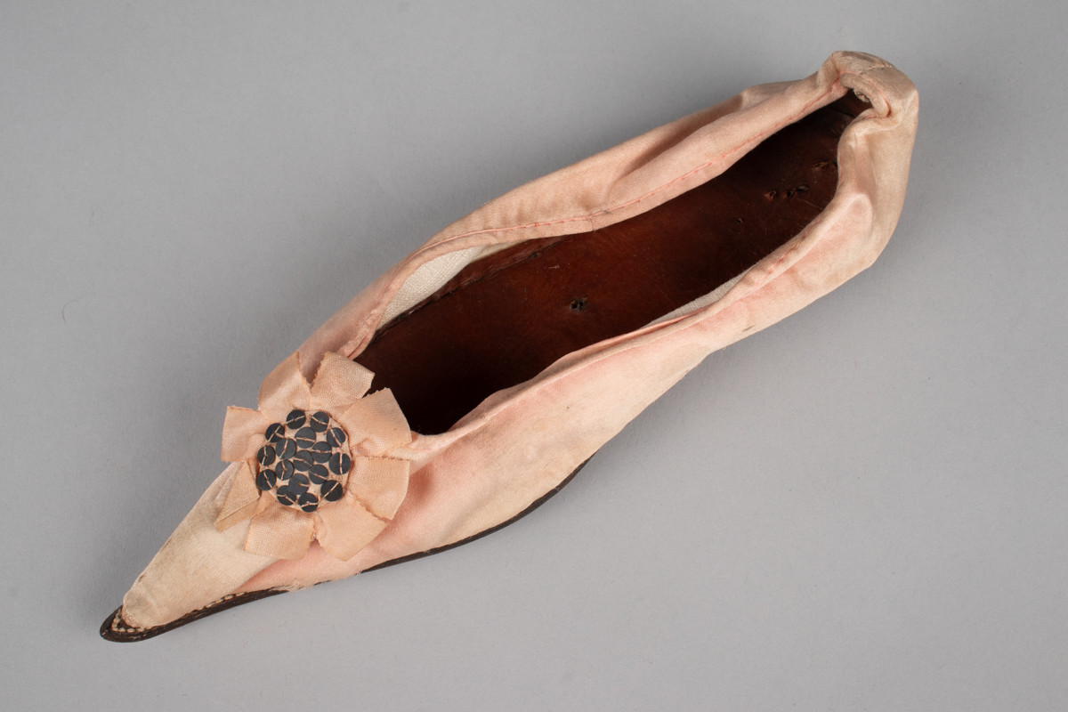 Rosa, håndsydd damesko eller tøffel i silke med spiss tå og flat lærsåle uten hæl. Dekorert med rosett med paljetter på rista.