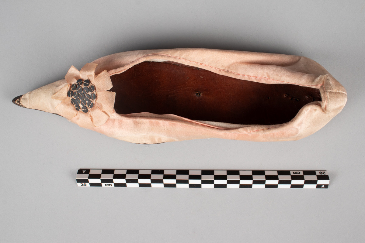 Rosa, håndsydd damesko eller tøffel i silke med spiss tå og flat lærsåle uten hæl. Dekorert med rosett med paljetter på rista.