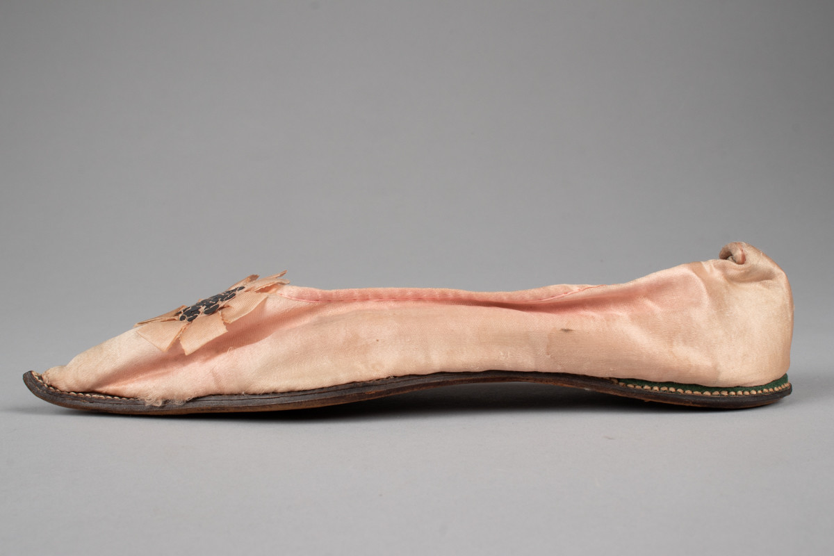 Rosa, håndsydd damesko eller tøffel i silke med spiss tå og flat lærsåle uten hæl. Dekorert med rosett med paljetter på rista.