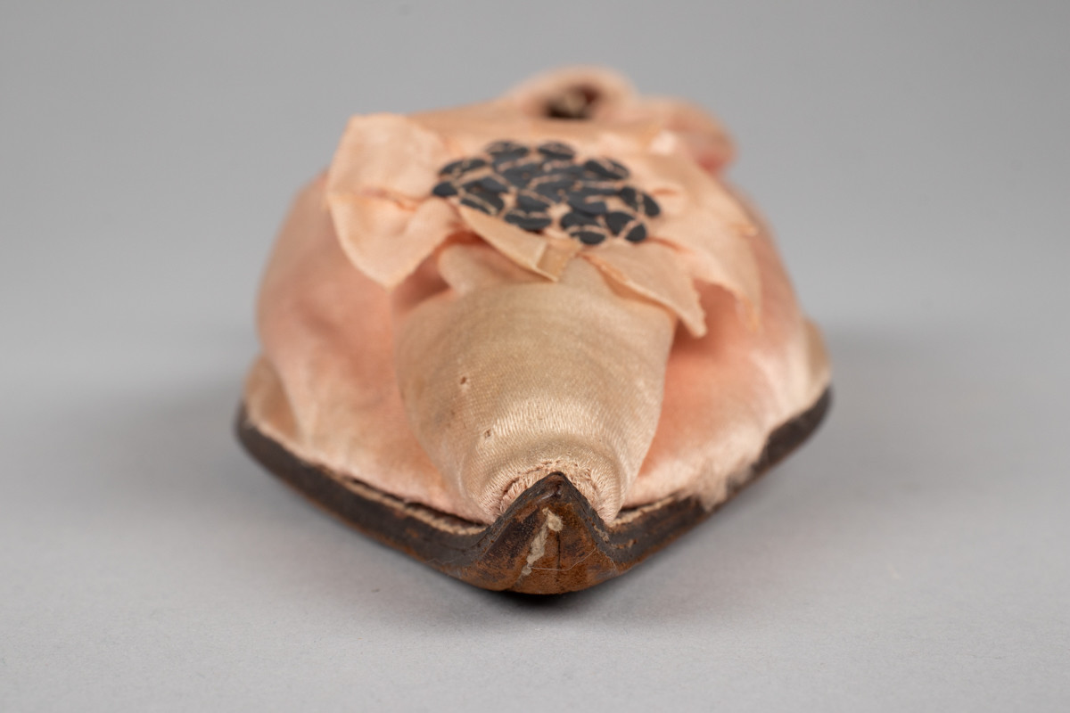 Rosa, håndsydd damesko eller tøffel i silke med spiss tå og flat lærsåle uten hæl. Dekorert med rosett med paljetter på rista.