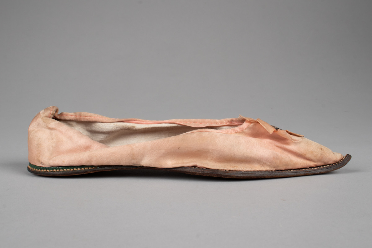 Rosa, håndsydd damesko eller tøffel i silke med spiss tå og flat lærsåle uten hæl. Dekorert med rosett med paljetter på rista.