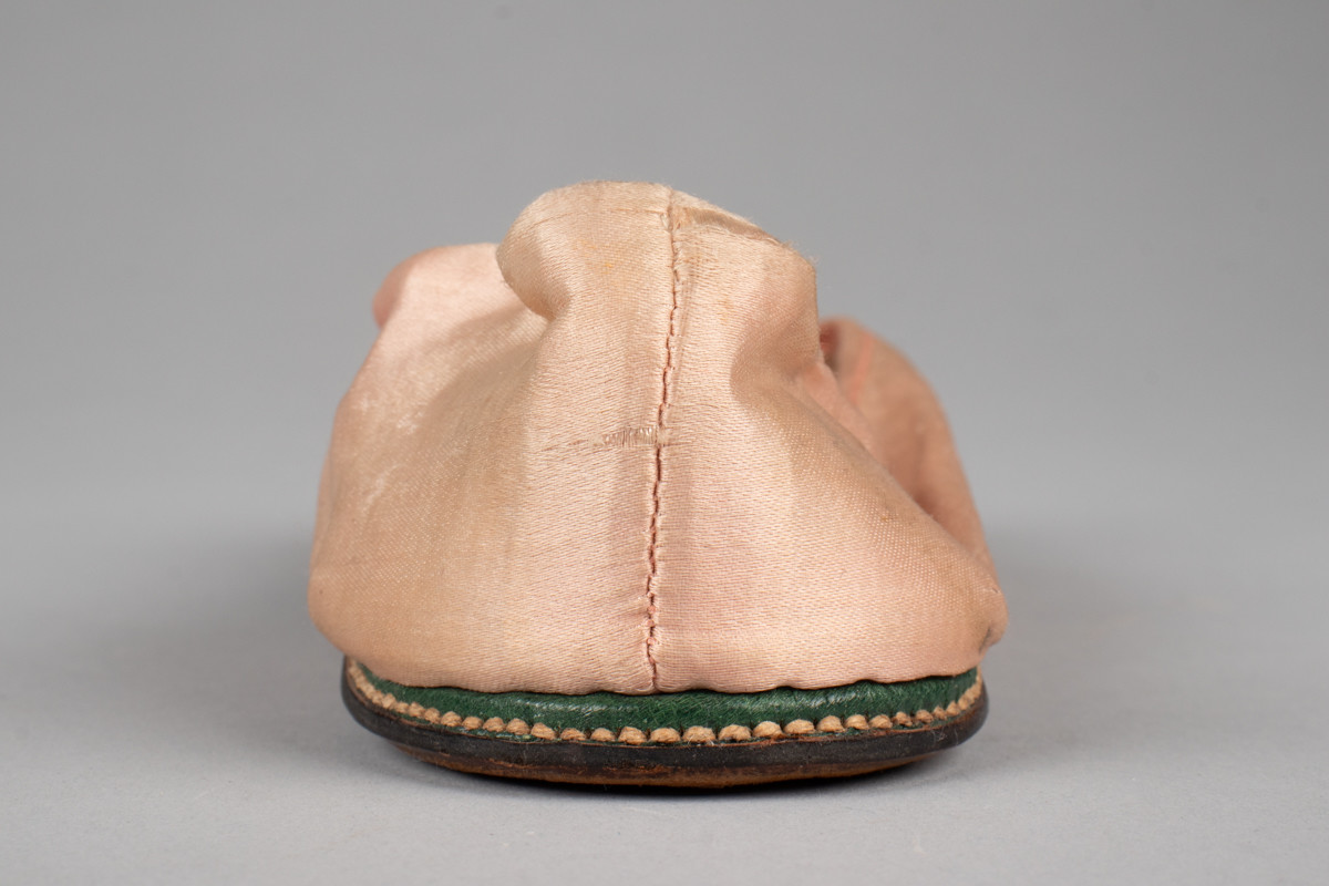 Rosa, håndsydd damesko eller tøffel i silke med spiss tå og flat lærsåle uten hæl. Dekorert med rosett med paljetter på rista.