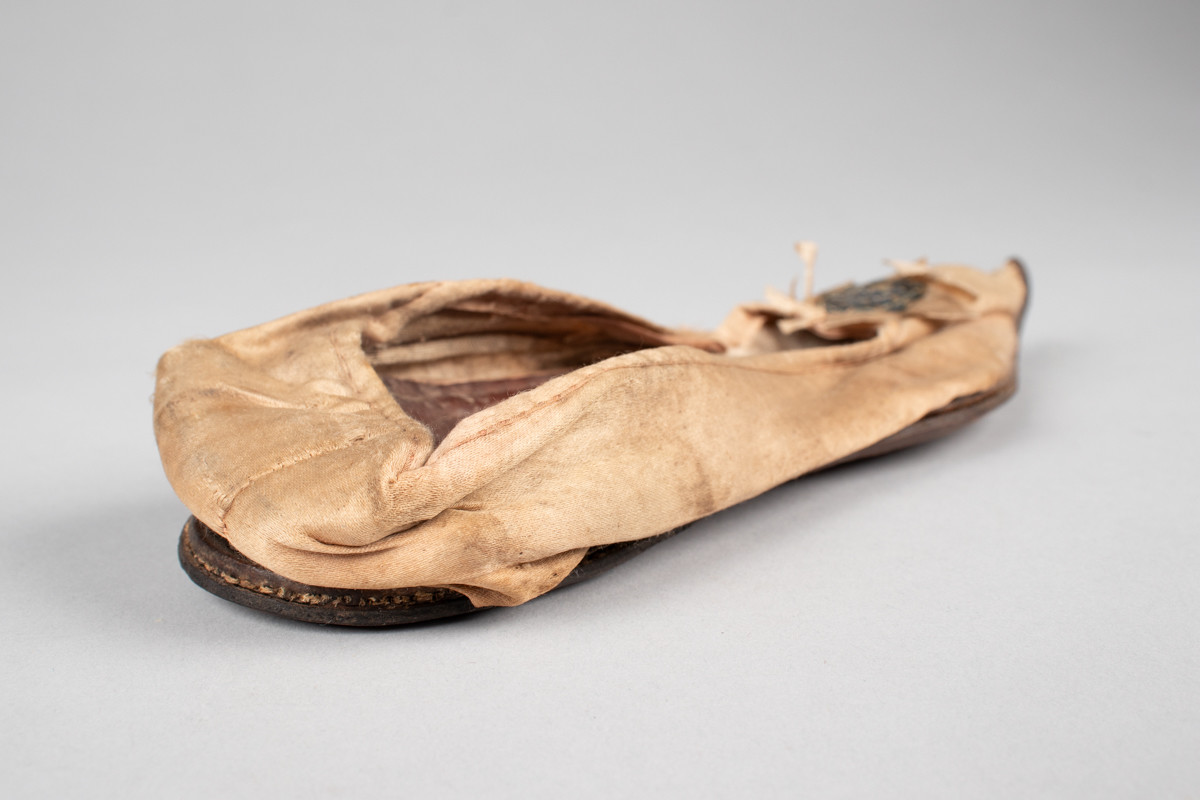 Rosa, håndsydd damesko eller tøffel i silke med spiss tå og flat lærsåle uten hæl. Dekorert med rosett med paljetter på rista.