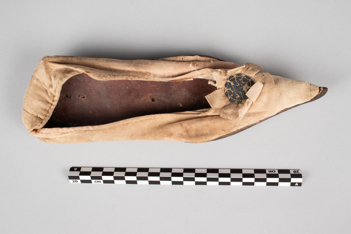 Rosa, håndsydd damesko eller tøffel i silke med spiss tå og flat lærsåle uten hæl. Dekorert med rosett med paljetter på rista.