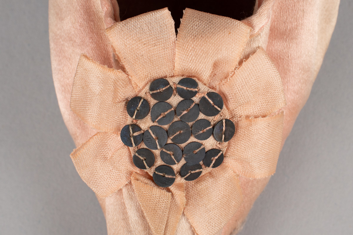 Rosa, håndsydd damesko eller tøffel i silke med spiss tå og flat lærsåle uten hæl. Dekorert med rosett med paljetter på rista.