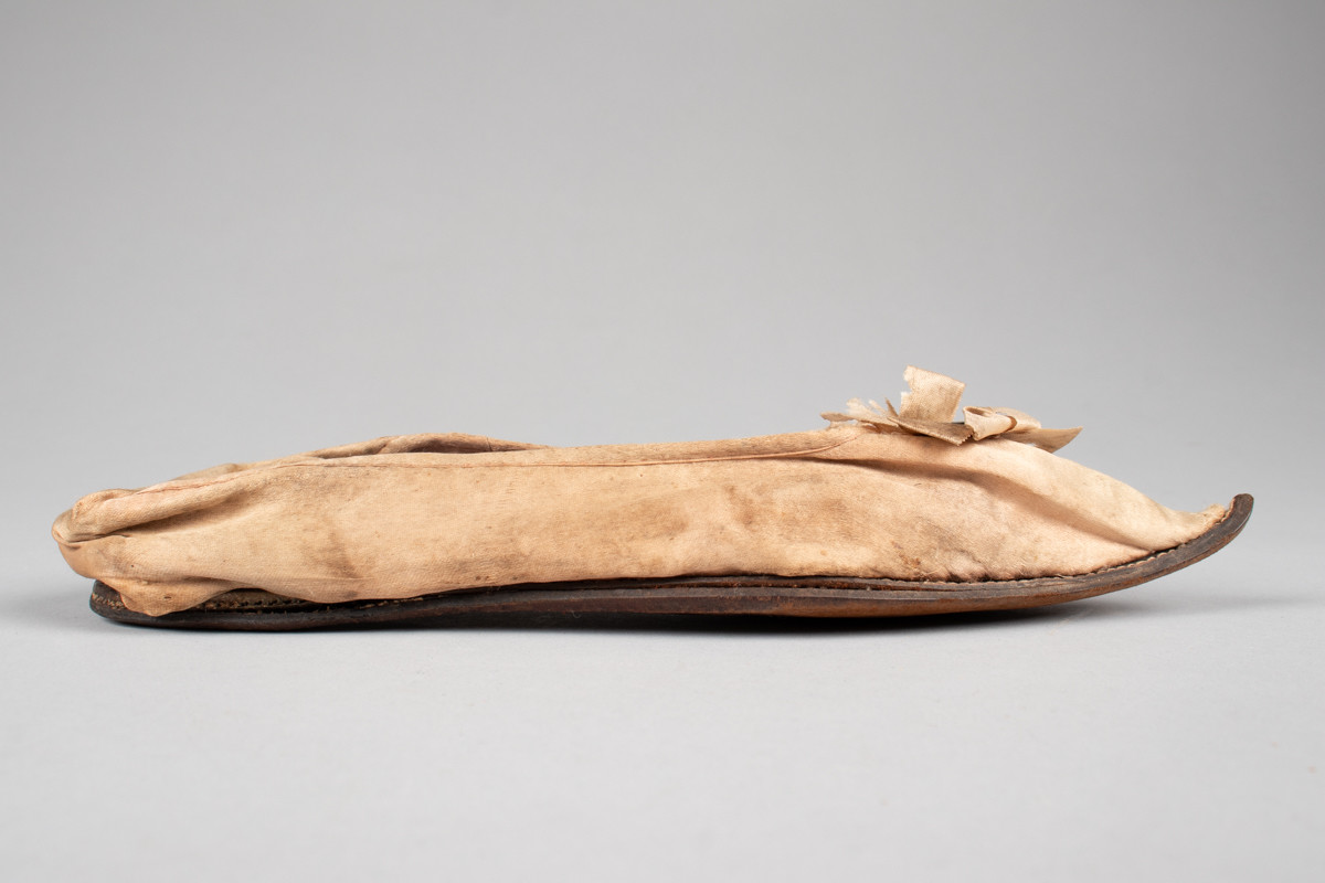 Rosa, håndsydd damesko eller tøffel i silke med spiss tå og flat lærsåle uten hæl. Dekorert med rosett med paljetter på rista.