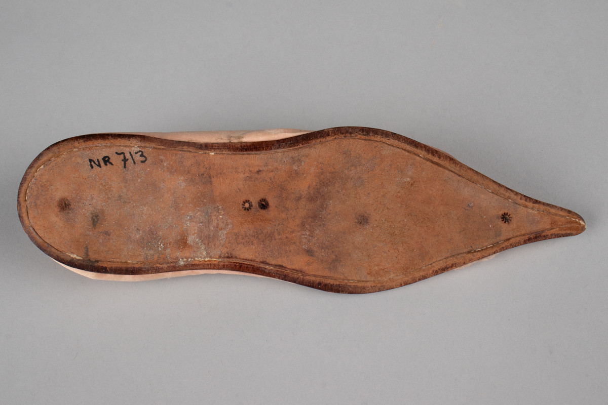 Rosa, håndsydd damesko eller tøffel i silke med spiss tå og flat lærsåle uten hæl. Dekorert med rosett med paljetter på rista.