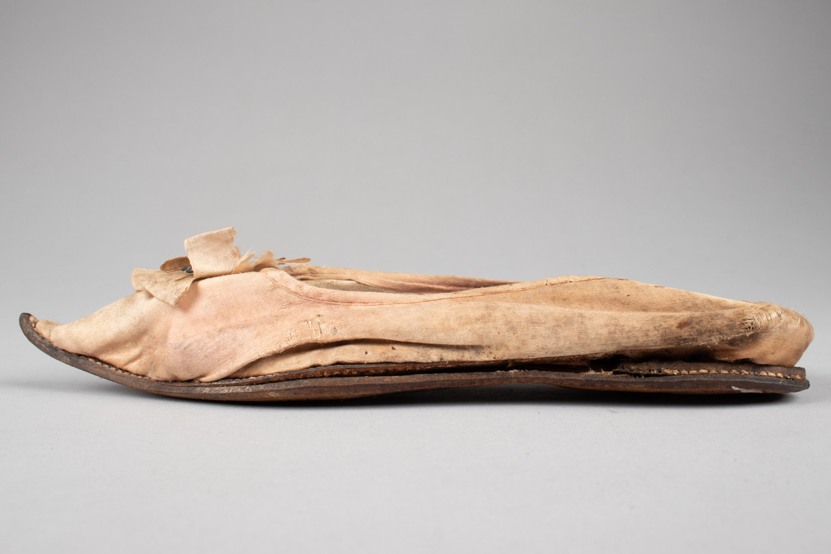 Rosa, håndsydd damesko eller tøffel i silke med spiss tå og flat lærsåle uten hæl. Dekorert med rosett med paljetter på rista.