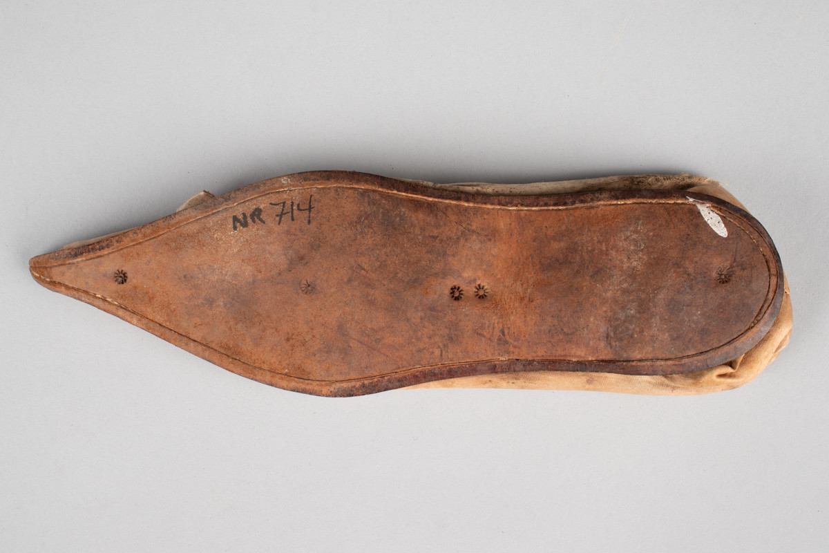 Rosa, håndsydd damesko eller tøffel i silke med spiss tå og flat lærsåle uten hæl. Dekorert med rosett med paljetter på rista.