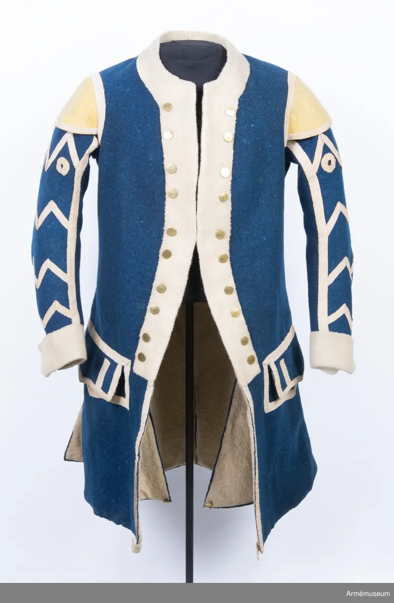 Rock av blått kläde med vita ärmuppslag och bröstrevärer av vitt kläde, gula axelkarmar, dekorationer av vävda vita band i tre olika bredder och släta mässingsknappar. Rocken är lång, med svängd mitt-fram-linje. Troligen nådde den nästan till knät på den som bar den. Den har 20 parvis ställda knappar fram, men knäpps kant i kant med två hyskor och hakar.
Den är konstruerad med hela framstycken som går runt till baksidan och bildar sidstycken. Delat bakstycke med mitt-bak-söm, samt tvåsömsärm. Sidsömmarna, ärmsömmarna och mitt-bak-sömmen är dekorerade med band. Två lågt ställda horisontella fickor fram med bandprydda ficklock, falska knapphål och två knappar vardera.
Skört med uppvik nertill fram. Sicksackdekorationer och rundlar på ärmarna.
Foder av vit boj i bålen, men oblekt bomull i ärmarna.