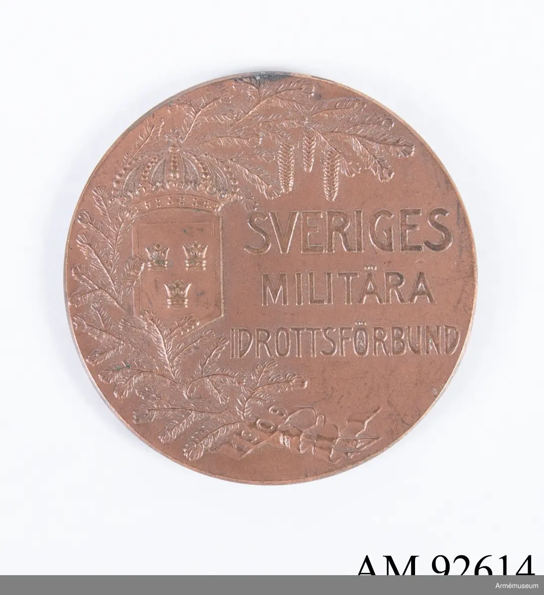 Medalj i koppar för Sveriges militära idrottsförbund.
I relief på framsidan syns en grankvist, riksvapnet och texten Sveriges Militära Idrottsförbund, samt årtalet 1909 i ett språkband nertill. 
På frånsidan syns idrottens beskyddarinna med lagerkvist i vänstra handen och en sköld med riksvapnet i högra handen. Frånsidan saknar text förutom tillverkarens namn C. G. Hallberg i liten stil längs med vänstra kanten.