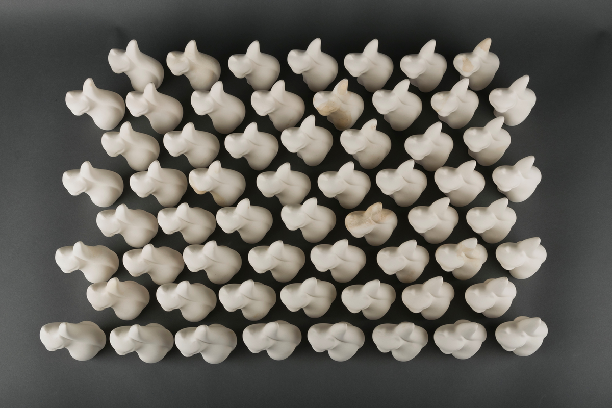 60 små katteskulpturer laget ved Egersunds Fayancefabrik. Skulpturene er udekorerte og uglaserte, og dermed ikke ferdigstilte produkter for salg.