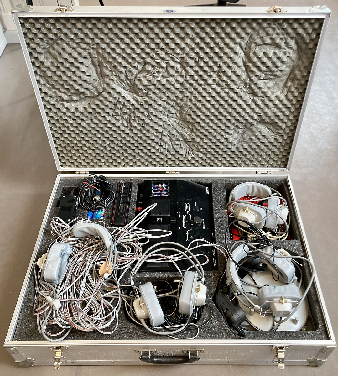 Koffert i metall som inneholder telefon og telefonsentral, opptaksutstyr og flere øretelefoner, lange telefonledninger, samt noe verktøy og kontorrekvisita, som skrujern, tapetkniv, tusjer, skrujern notatpapir, stifter, ekstra batterier mm.