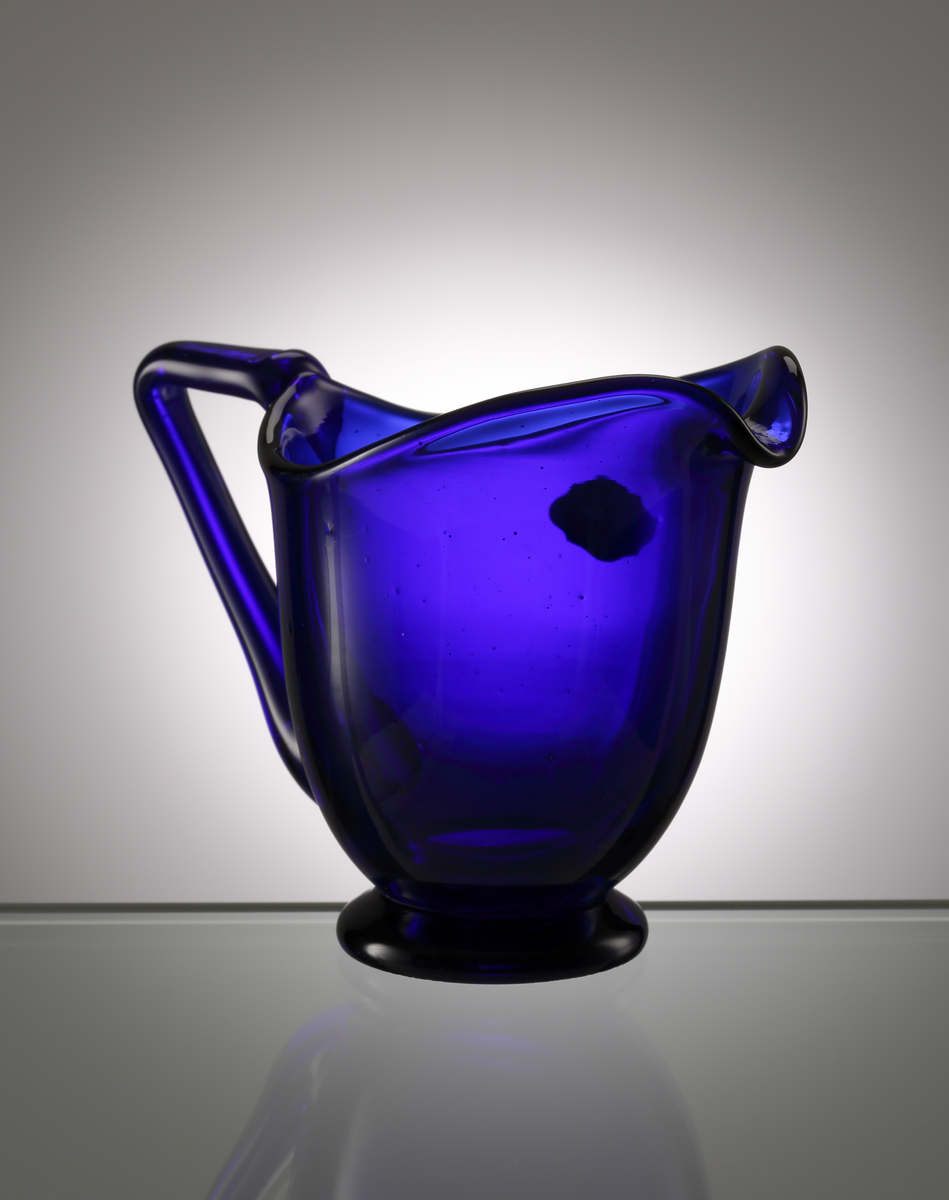 Koboltblå gräddkanna på klack. Grep och snip. Etikett: KALMAR GLASBRUK SWEDEN.