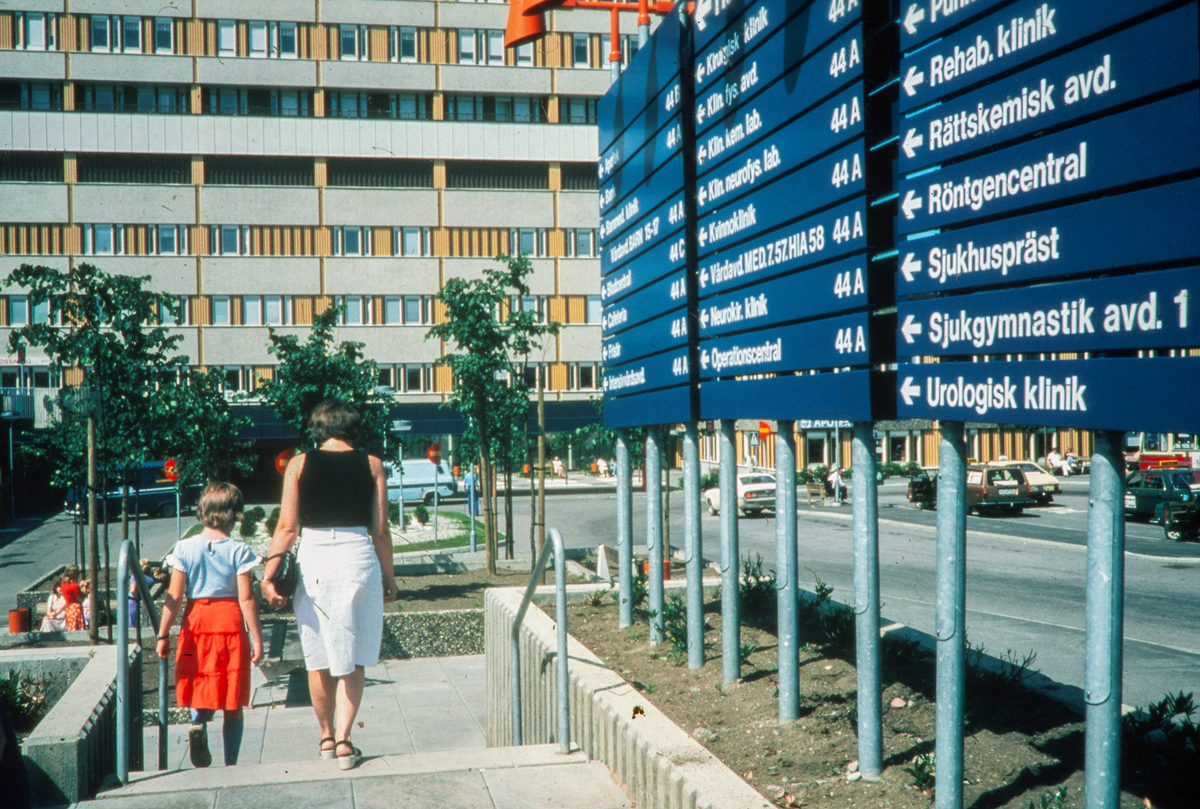 Norra entrén på Universietssjukhuset i Linköping. Huvudblocket. 
Sjukhus. Man ser en kvinna och ett barn på väg mot sjukhuset. 
Bilder från staden Linköping digitaliserade från diapositiv. Bilderna är från 1970-1990-talet.