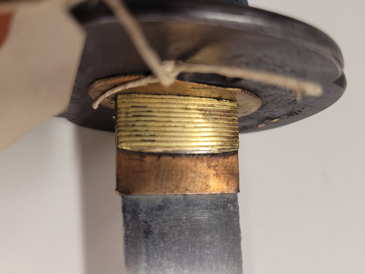 Samurai-dolk (WAKICACHI) från Japan. Klinga svagt bakåtböjd,eneggad, skarp, facetterad rygg. Fäste av vitt hajskinn flätat med grönt bomullsband med två amuletter, delvis förgyllda. Beslag upptill och nedtill cicilerade och förgyllda. Parerplåt rund med ett hål på ena sidan samt med förgyllt och cicilerat bladverk. Balja av trä, svartlackerad med beslag å fyra ställen.
Låsfjädern,d.v.s. bestickknivens handtag saknas.
Kniven på baljan (KOZUKA) saknas.
Från fregatten VANADIS världsomsegling 1883-85.