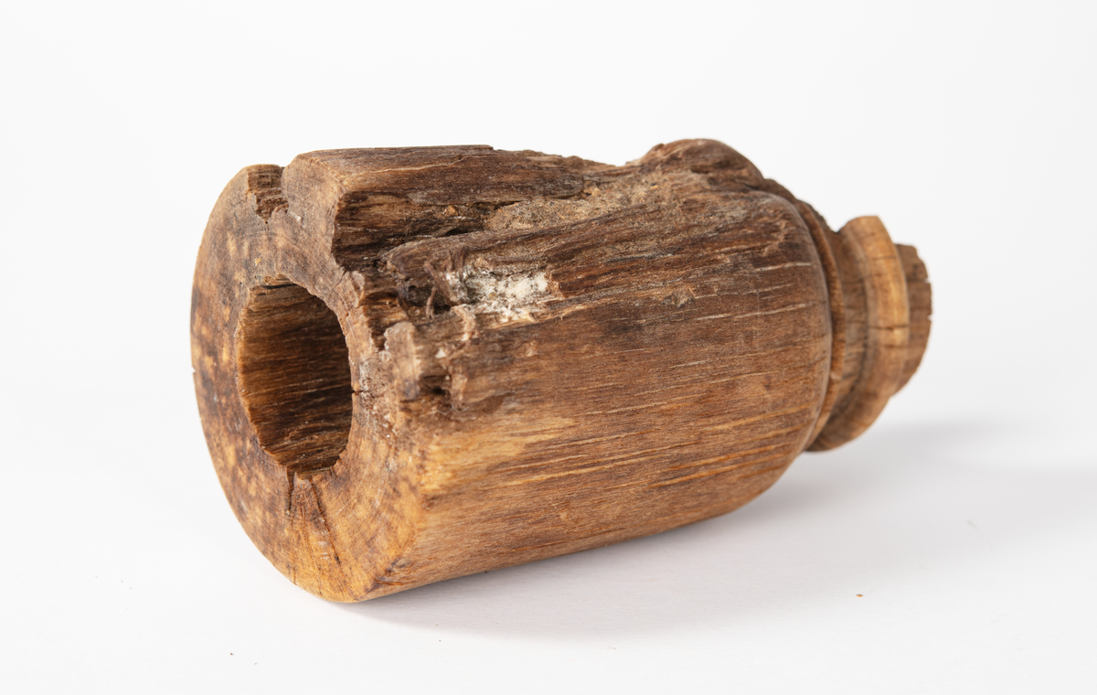 Ansättare som är snyggt svarvad. Hål för skaft mäter 27 mm. Trät som smör, delar av ytan faller sönder. Skadad på en sida. Rest av materialet i skafthålet undersöktes under arbetsmikroskop för att utesluta att det var något som tillhörde föremålet. Består av sediment med organiskt material. Prov sparat i påse.