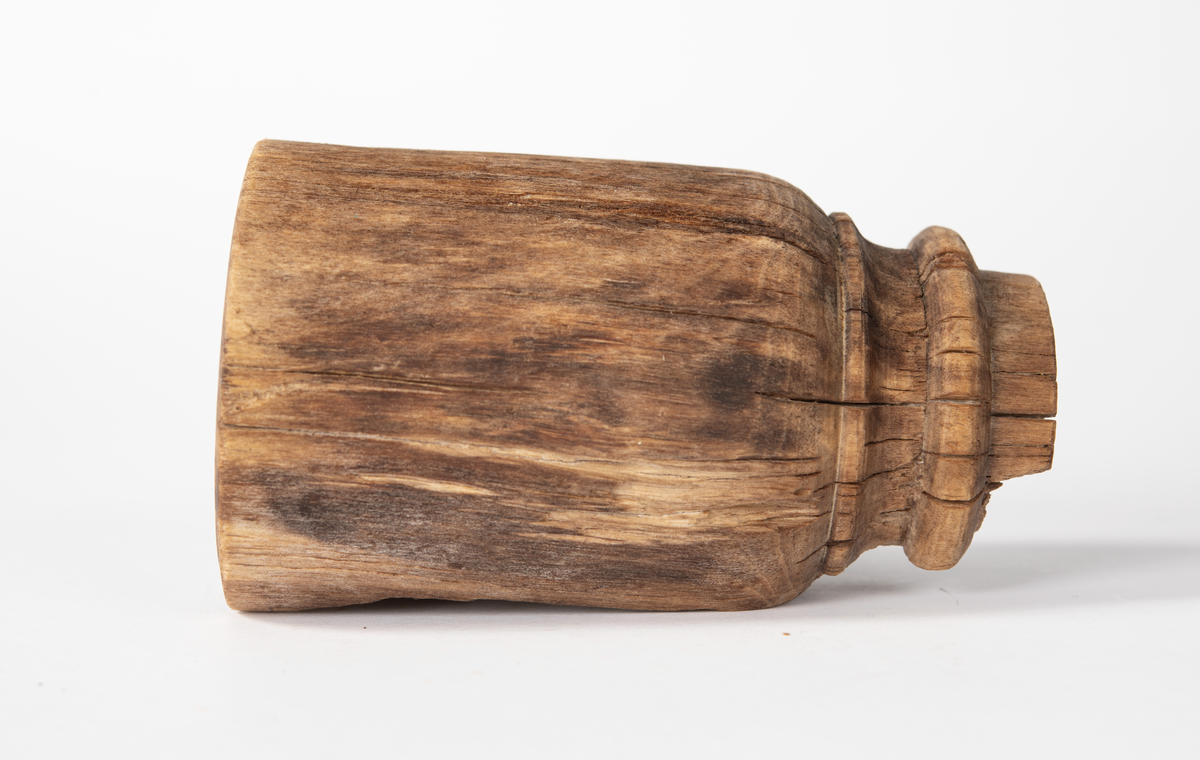 Ansättare som är snyggt svarvad. Hål för skaft mäter 27 mm. Trät som smör, delar av ytan faller sönder. Skadad på en sida. Rest av materialet i skafthålet undersöktes under arbetsmikroskop för att utesluta att det var något som tillhörde föremålet. Består av sediment med organiskt material. Prov sparat i påse.