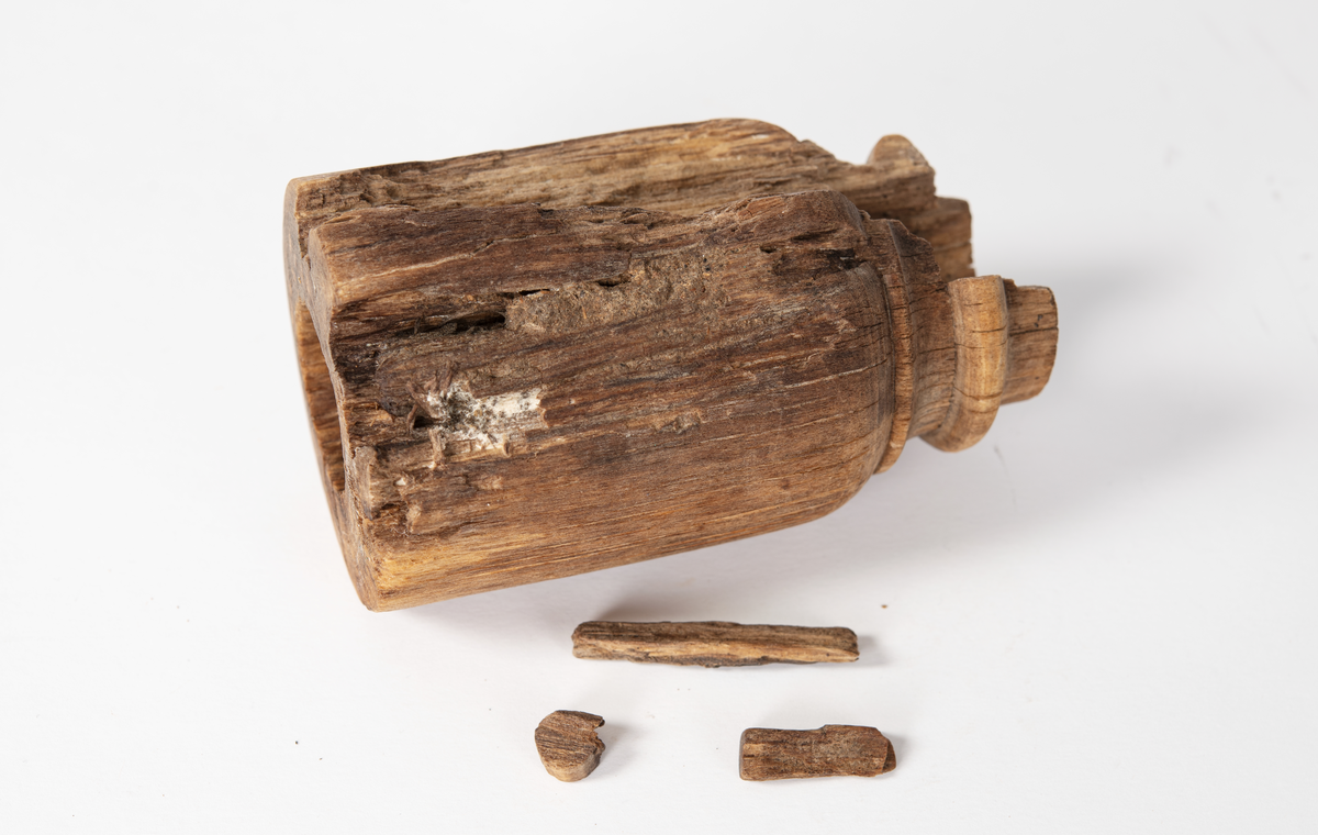 Ansättare som är snyggt svarvad. Hål för skaft mäter 27 mm. Trät som smör, delar av ytan faller sönder. Skadad på en sida. Rest av materialet i skafthålet undersöktes under arbetsmikroskop för att utesluta att det var något som tillhörde föremålet. Består av sediment med organiskt material. Prov sparat i påse.