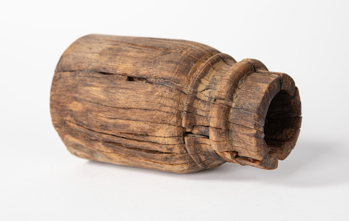 Ansättare. Sprucken i fyra delar. Hål för skaft 27 mm. Trät som smör, delar av ytan faller sönder. Nagg i kant. Kraftig sprickbildning.