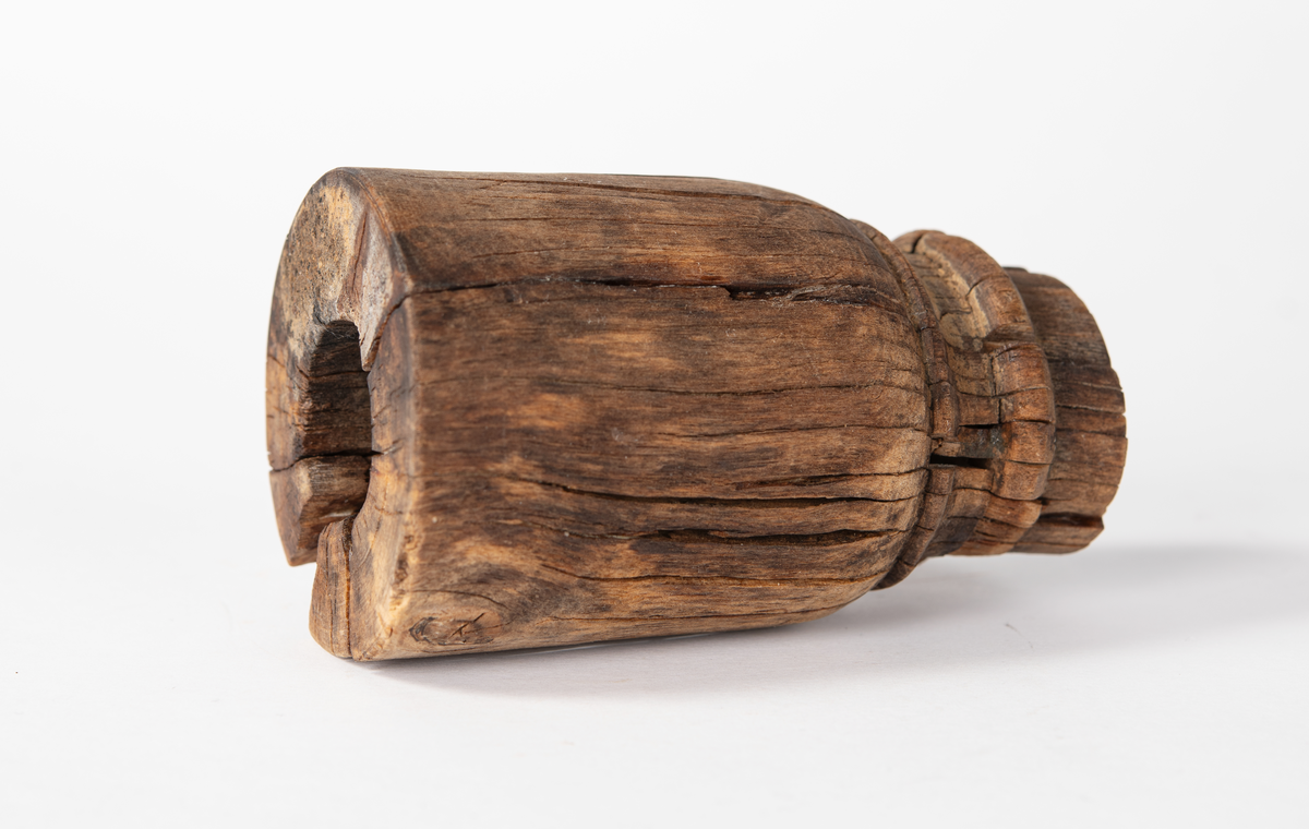 Ansättare. Sprucken i fyra delar. Hål för skaft 27 mm. Trät som smör, delar av ytan faller sönder. Nagg i kant. Kraftig sprickbildning.