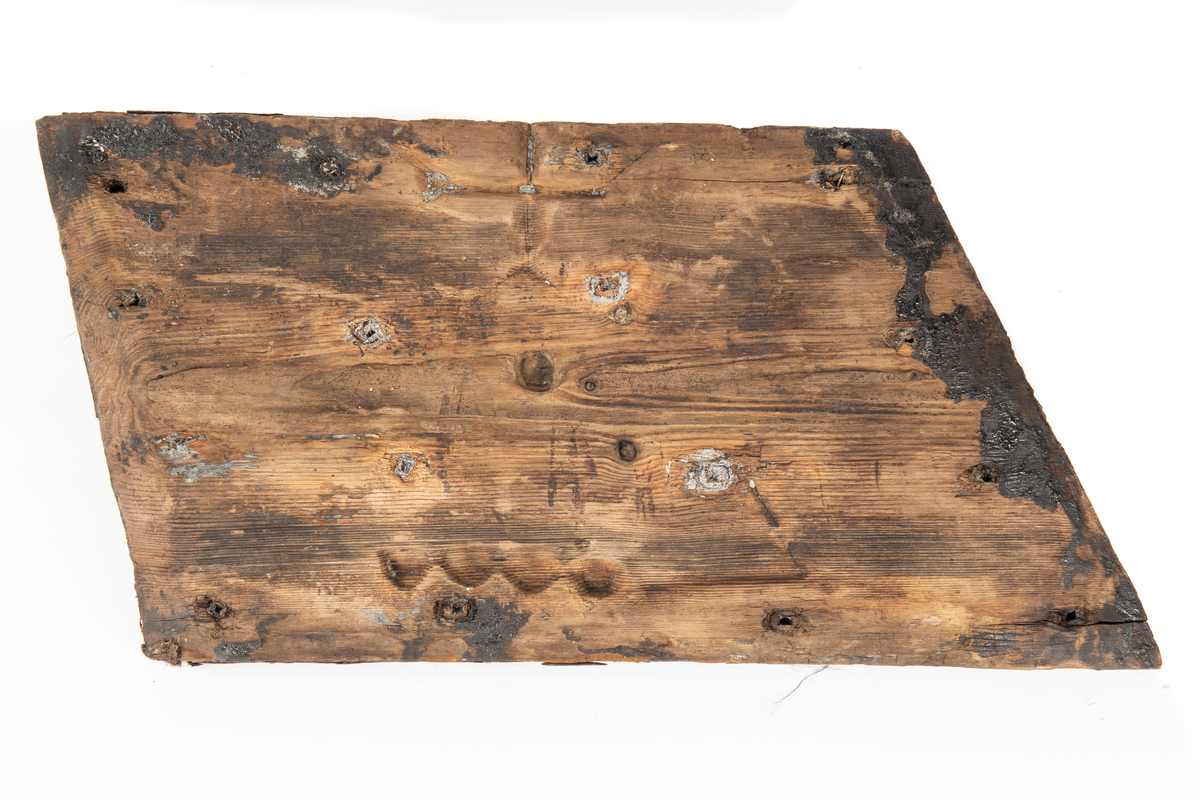 Del av fyrhydning eller extra skrov med rester av fibermatta. Möjligen rester av spik i spikhålen. Mycket järn i ytan på i synnerhet på ytan inåt med rester av fibrer.