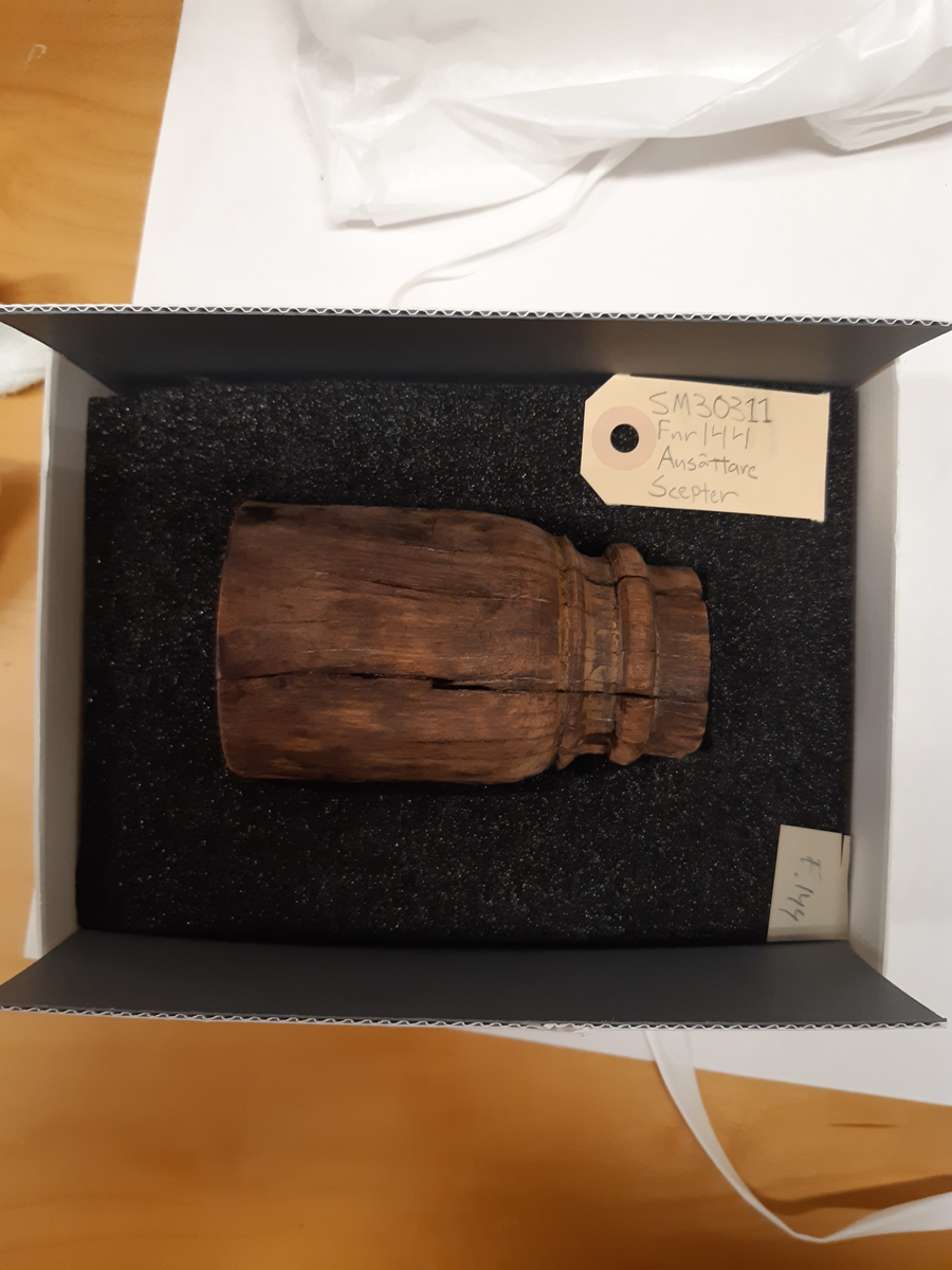 Ansättare. Sprucken i fyra delar. Hål för skaft 27 mm. Trät som smör, delar av ytan faller sönder. Nagg i kant. Kraftig sprickbildning.