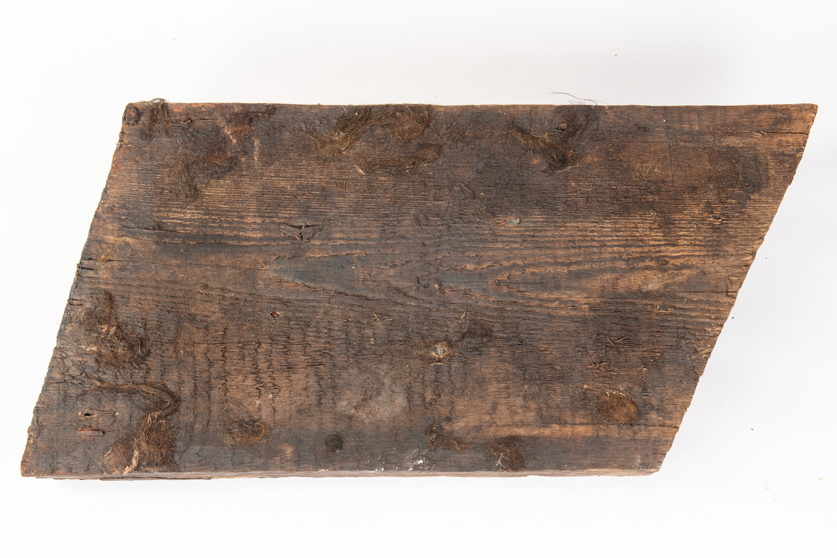 Del av fyrhydning eller extra skrov med rester av fibermatta. Möjligen rester av spik i spikhålen. Mycket järn i ytan på i synnerhet på ytan inåt med rester av fibrer.