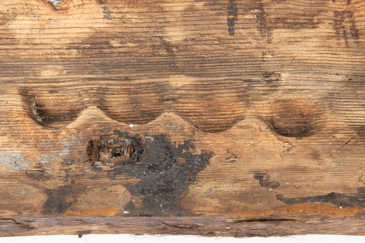 Del av fyrhydning eller extra skrov med rester av fibermatta. Möjligen rester av spik i spikhålen. Mycket järn i ytan på i synnerhet på ytan inåt med rester av fibrer.