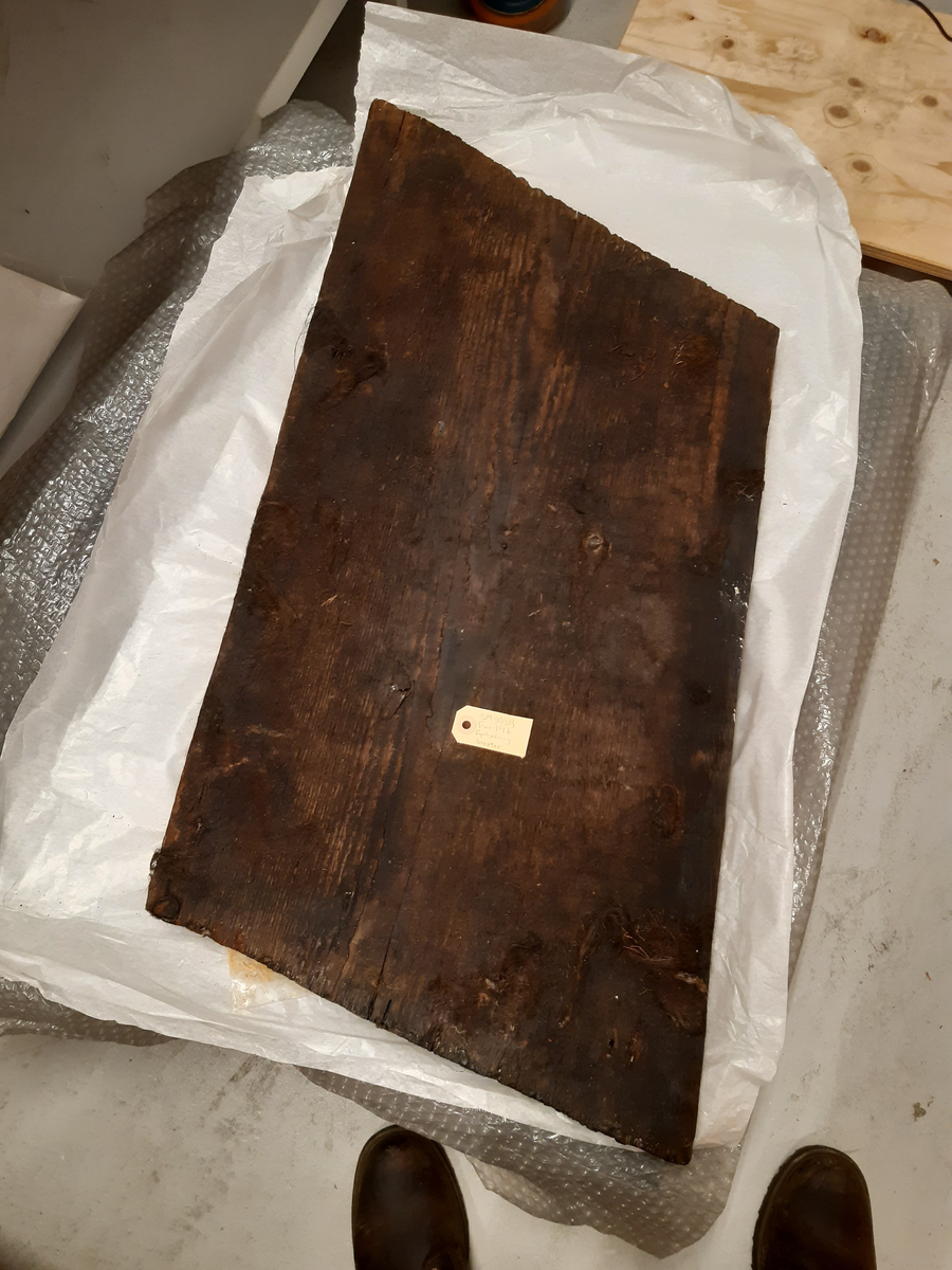 Del av fyrhydning eller extra skrov med rester av fibermatta. Möjligen rester av spik i spikhålen. Mycket järn i ytan på i synnerhet på ytan inåt med rester av fibrer.