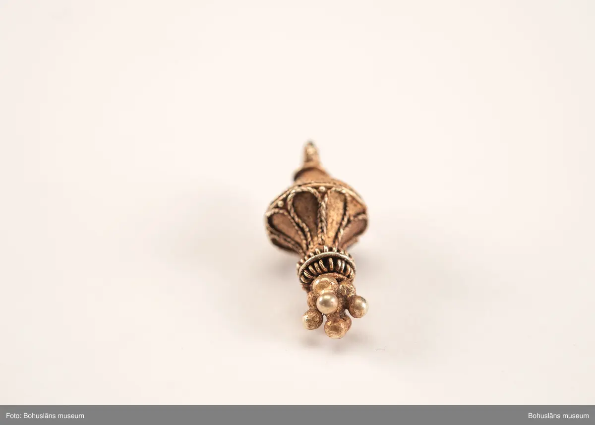 Ett utsökt intakt hängsmycke av guld, en s k päronformad berlock. Överst på hänget, finns en ögla för upphängning på ett band, halskedja eller liknande. Dekoren är utförd i s k filigranteknik, och visar på högt hantverksmässigt kunnande. Mycket tunna, tvinnade eller flätade guldtrådar är lagda ovanpå och runt hängets övre del. På hängets undre del är flera små runda guldkulor (granuleringar) fästade. Berlocken tillhör "typ III", enligt von Müllers typologi (se Müller 1958). Formmässigt har hänget sitt ursprung i östra Medelhavet och området kring Svarta havet.

Denna typ av hängsmycken är mycket ovanligt att hitta i våra trakter, det är endast en handfull som tidigare påträffats i Sverige och de flesta på Öland. Desto fler har däremot hittats i Danmark (se Rapport 2020:166, s.12).

Hänget/berlocken hittades, tillsammans med fyra spännen av brons, ett 40-tal keramikskärvor, brända och obrända ben, däribland en tand, flintavslag och bitar av en dekorerad kam av horn. Graven innehöll två individer. Den ena var jordlagd utan kremering och den andra kremerad. Den jordlagda individen hade endast ett fåtal ben och tänder bevarade. De visade sig tillhöra en ung person, ca 16-20 år gammal. Förmodligen en kvinna, vilket de gravgåvor som var nedlagda i graven visade.
Den andra individen, till vilken de brända benen hörde, var även det en ung person. 
För mer info om, och tolkning av fyndet se rapport Arkeologerna 2020:166.