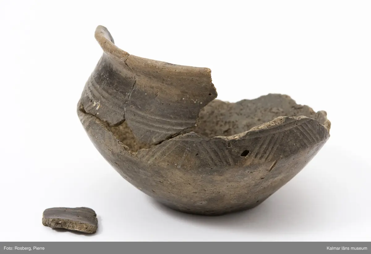 KLM 7393. Gravurna. Av lera med ornament av sicksacklinjer. Buken skarpt bruten.