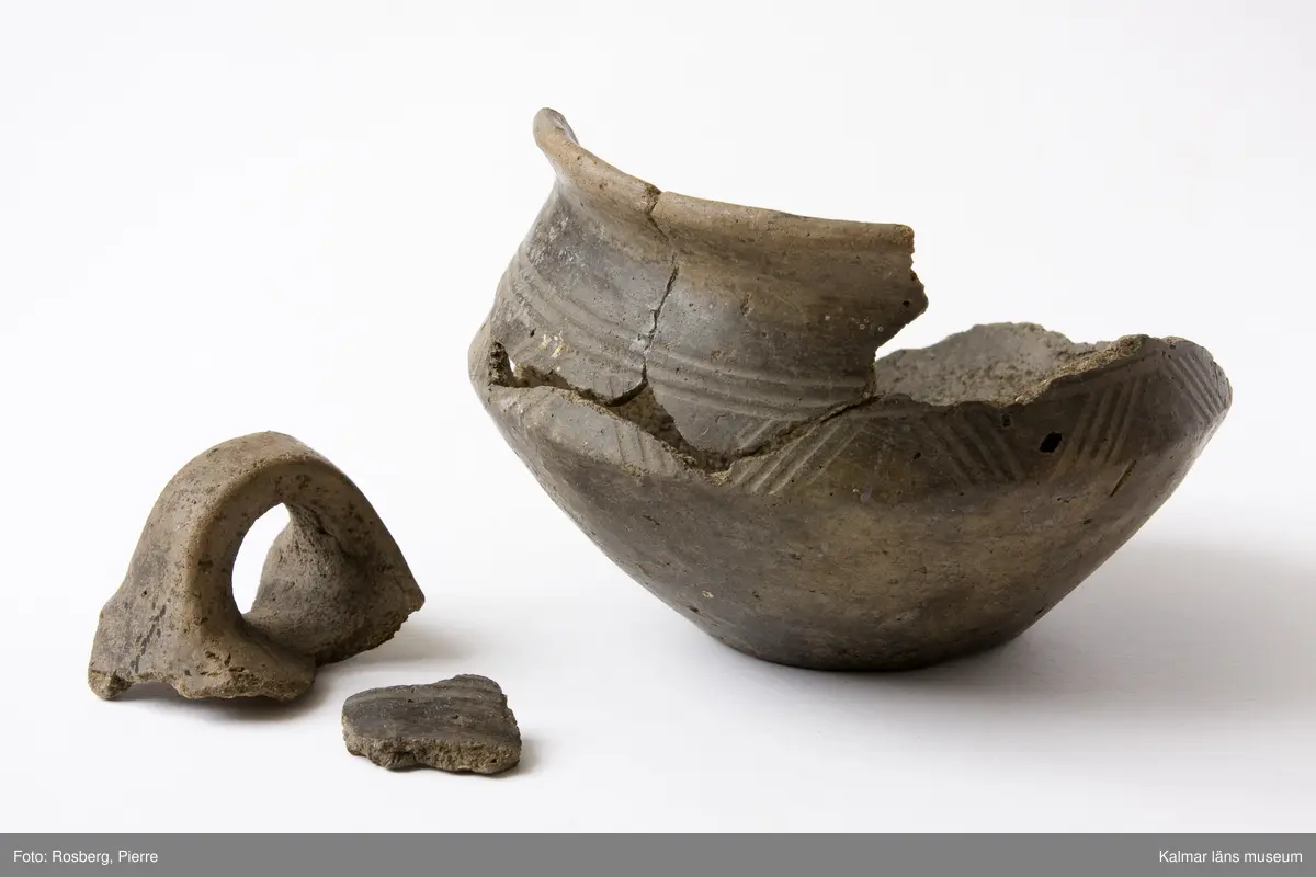 KLM 7393. Gravurna. Av lera med ornament av sicksacklinjer. Buken skarpt bruten.