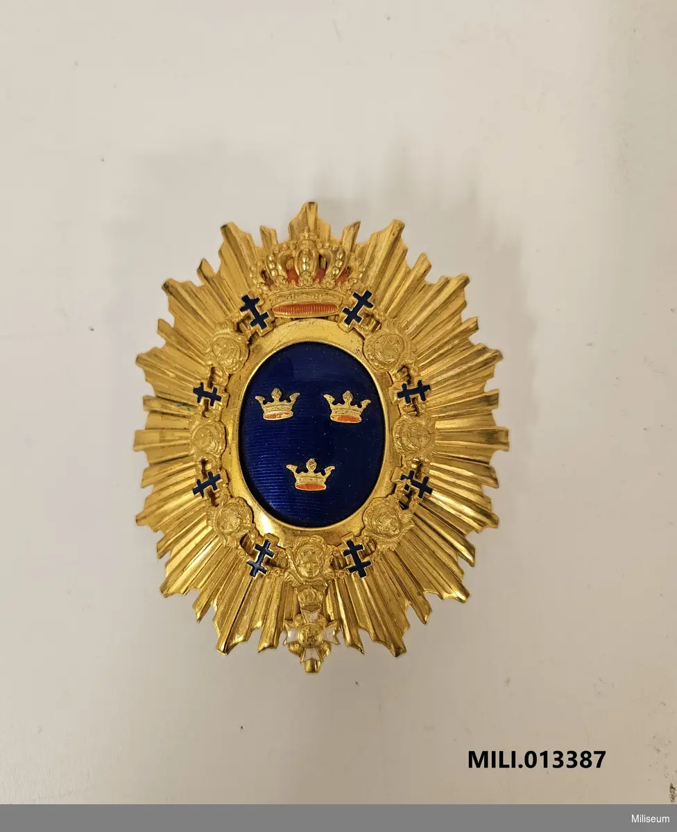 Emblem m/1880 till käppi m/1880, av förgylld mässing. Med fastlödd pompong.