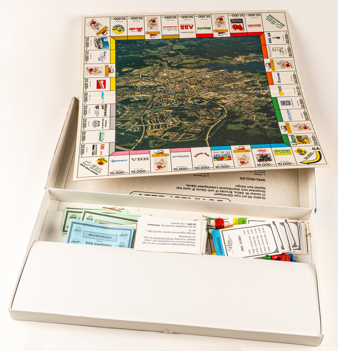 Sällskapsspel i kartong, innehållande spelplan med karta över Gävle, tärningar och spelpjäser i trä samt olika spelkort. 
I locket spelregler för LOKALSPELET GÄVLE.