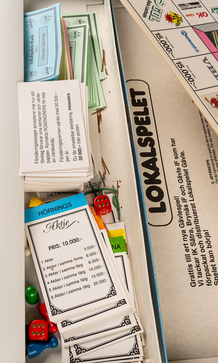 Sällskapsspel i kartong, innehållande spelplan med karta över Gävle, tärningar och spelpjäser i trä samt olika spelkort. 
I locket spelregler för LOKALSPELET GÄVLE.