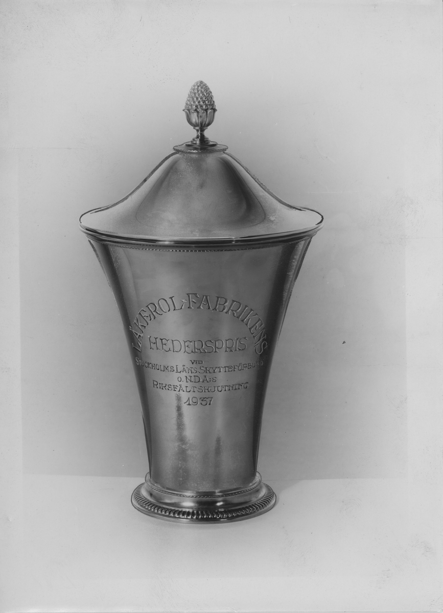 Silverpokal med lock.
Gravyr på pokalen lyder: "Läkerolfabrikens hederspris vid Stockholmsläns skytteförbund o NDA:s Riksfältskjutning 1957."