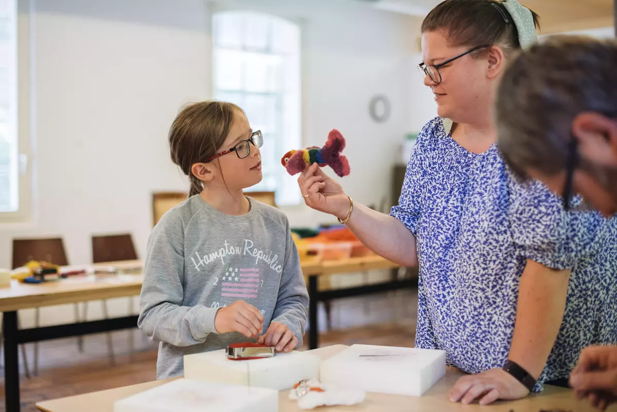 En voksen viser en fiskefigur i ull til en jente.